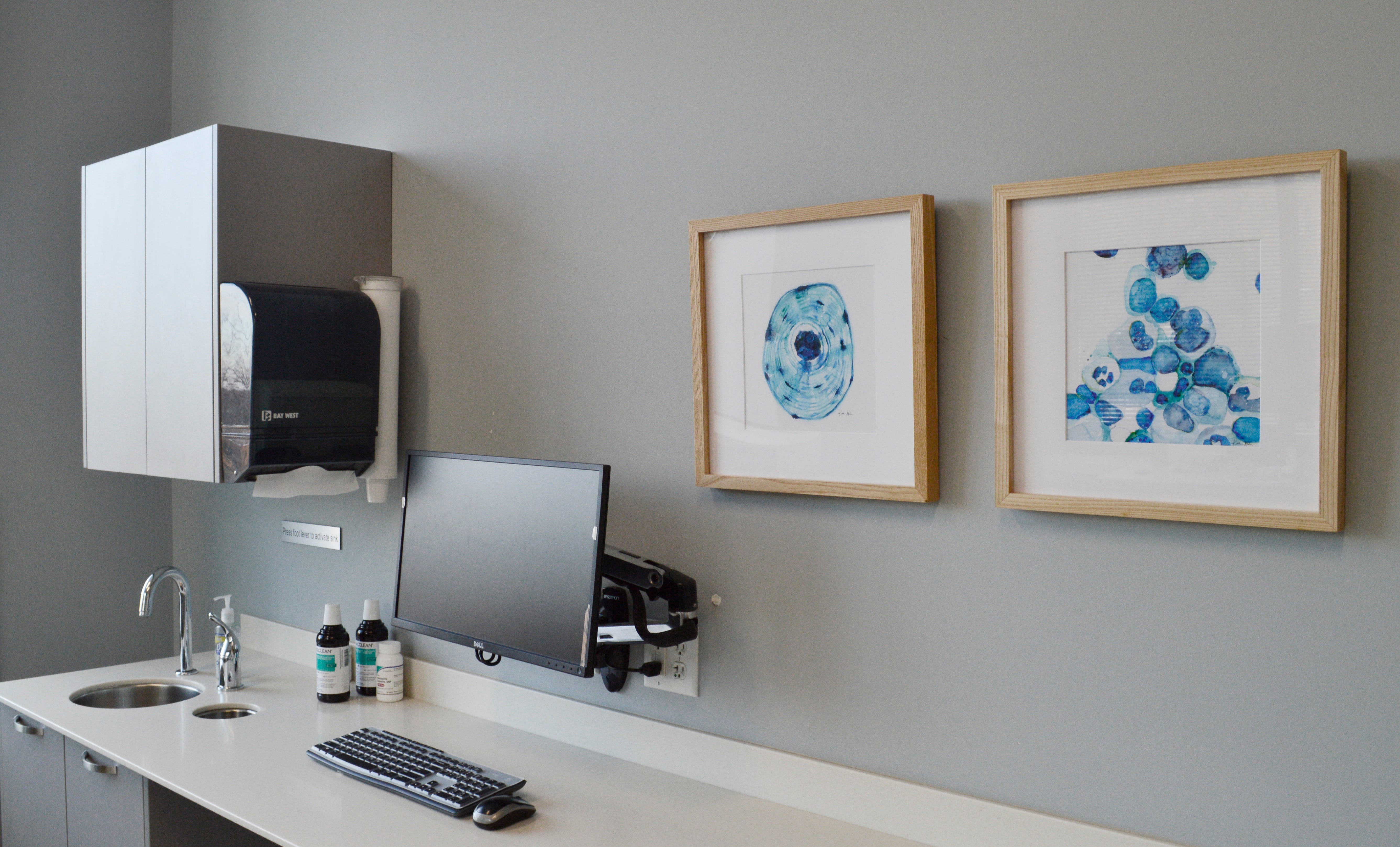 Modern doctor office setup with a desk, computer monitor, and framed anatomy artwork on a gray wall.