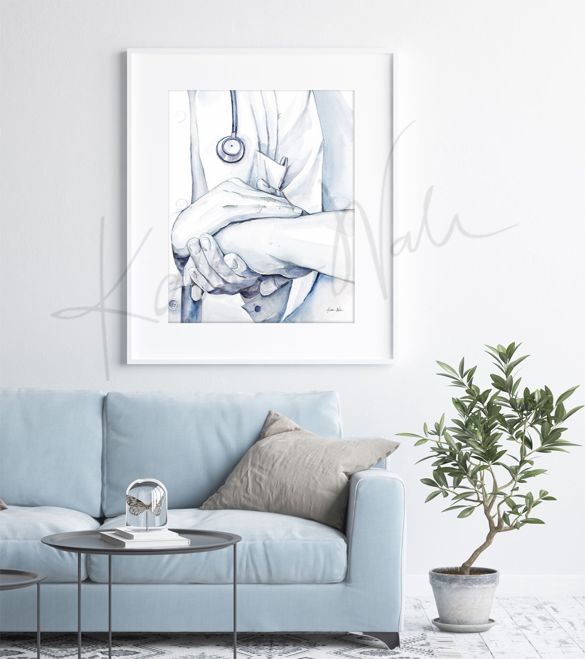 Framed watercolor painting of a doctor holding a patient’s hand in comfort. The painting is hanging over a blue couch