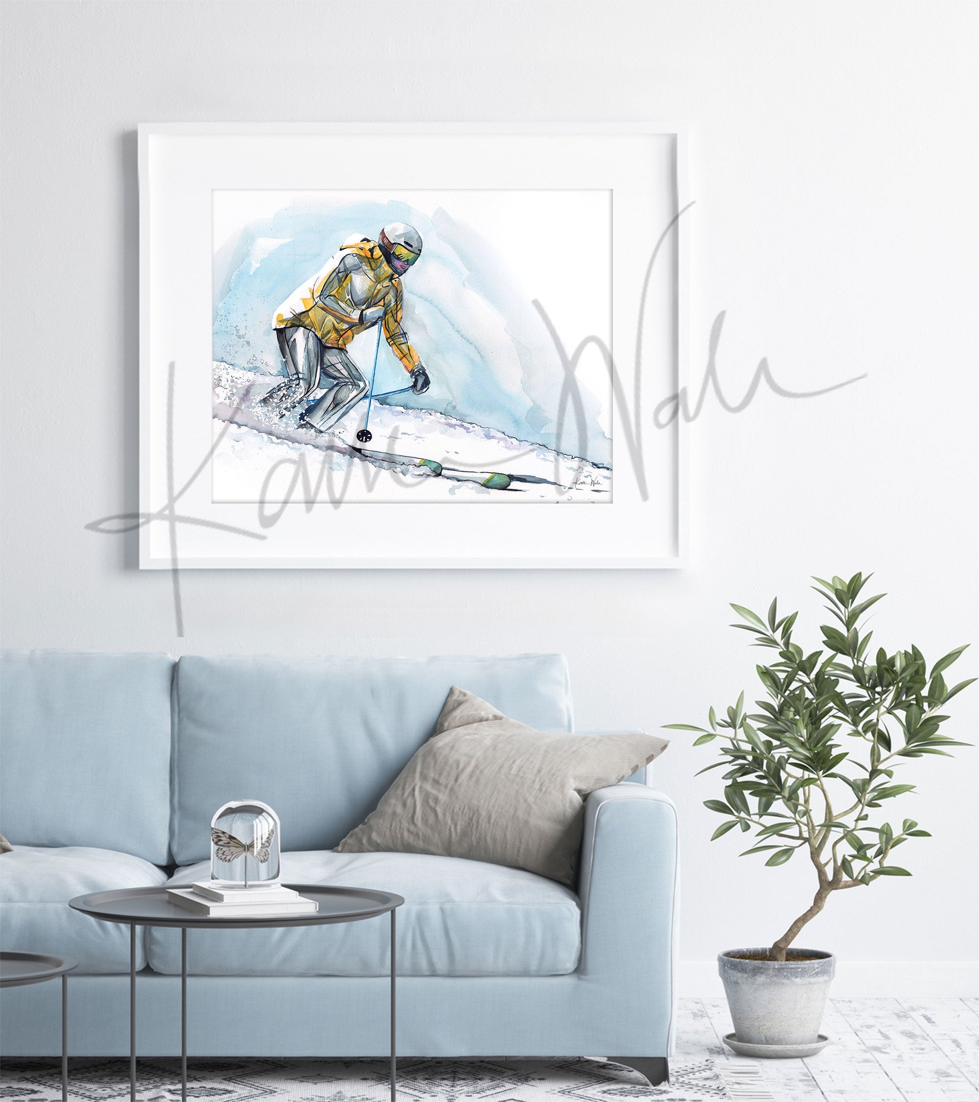 Framed watercolor painting of a skier going down a ski hill with their muscle anatomy showing under their clothing. The painting is hanging over a blue couch.