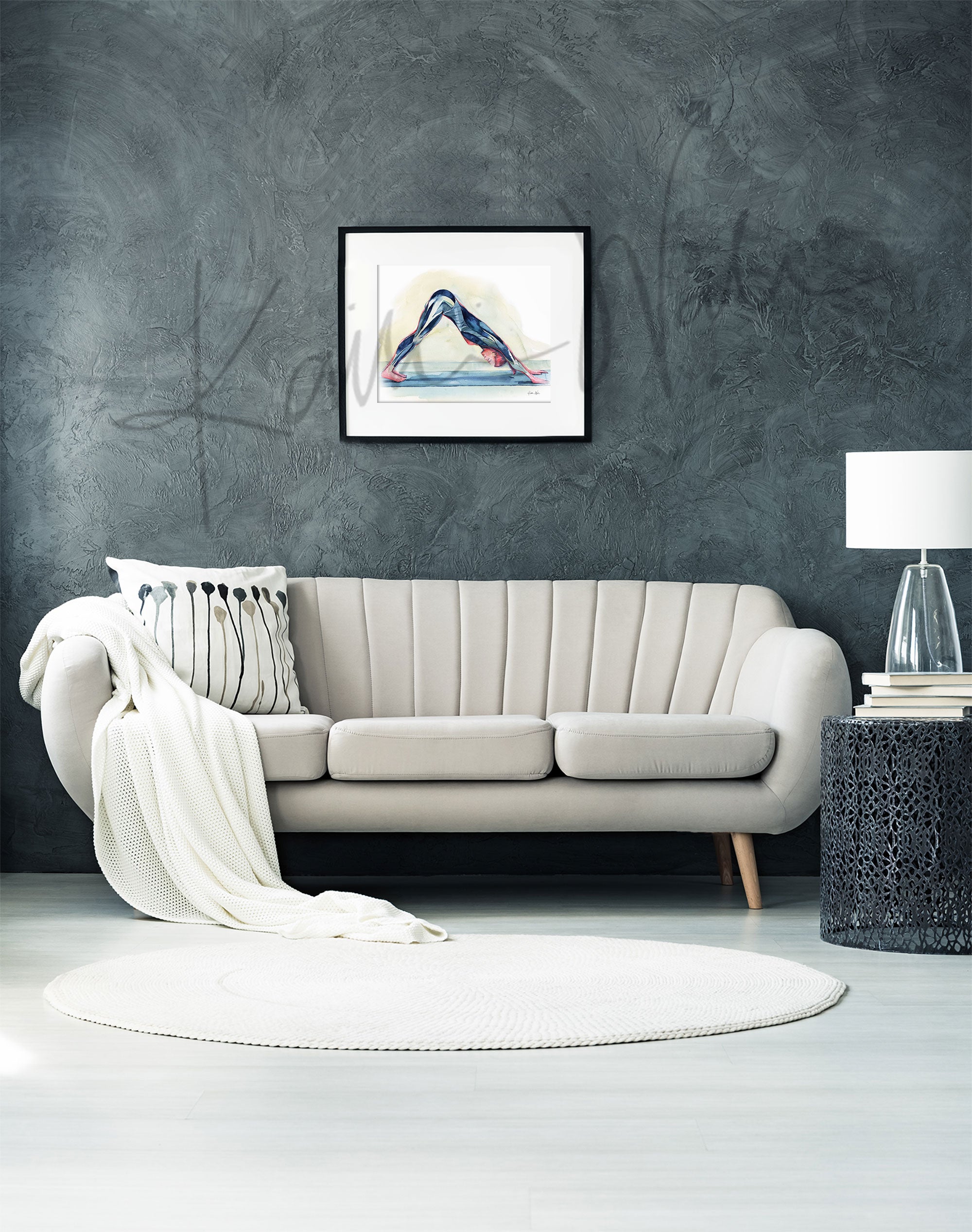 Framed watercolor painting of a woman doing a down dog yoga pose and shows her muscular anatomy within the pose. The painting is hanging over a white couch.