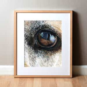 Framed watercolor painting of a zoomed in perspective of a dog’s eye. The painting is in blacks, tans, and browns.