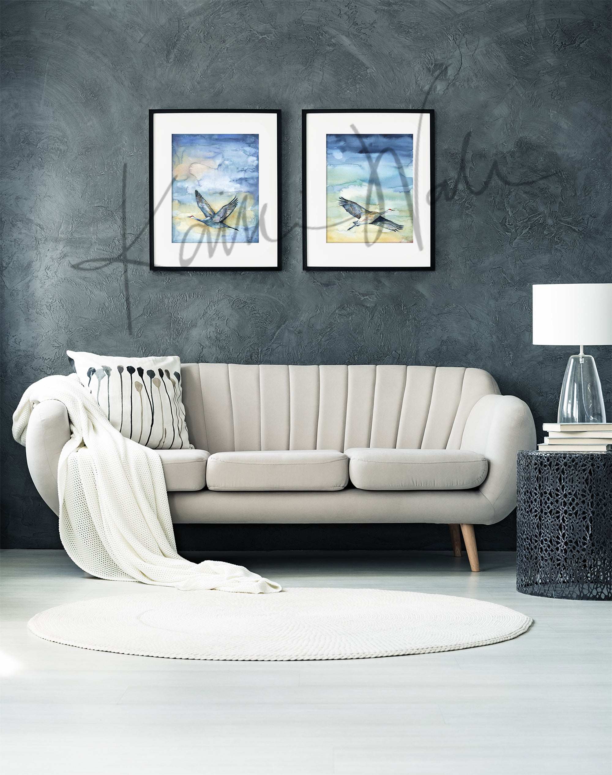 Framed watercolor painting set of flying cranes. The paintings are hanging over a beige couch.