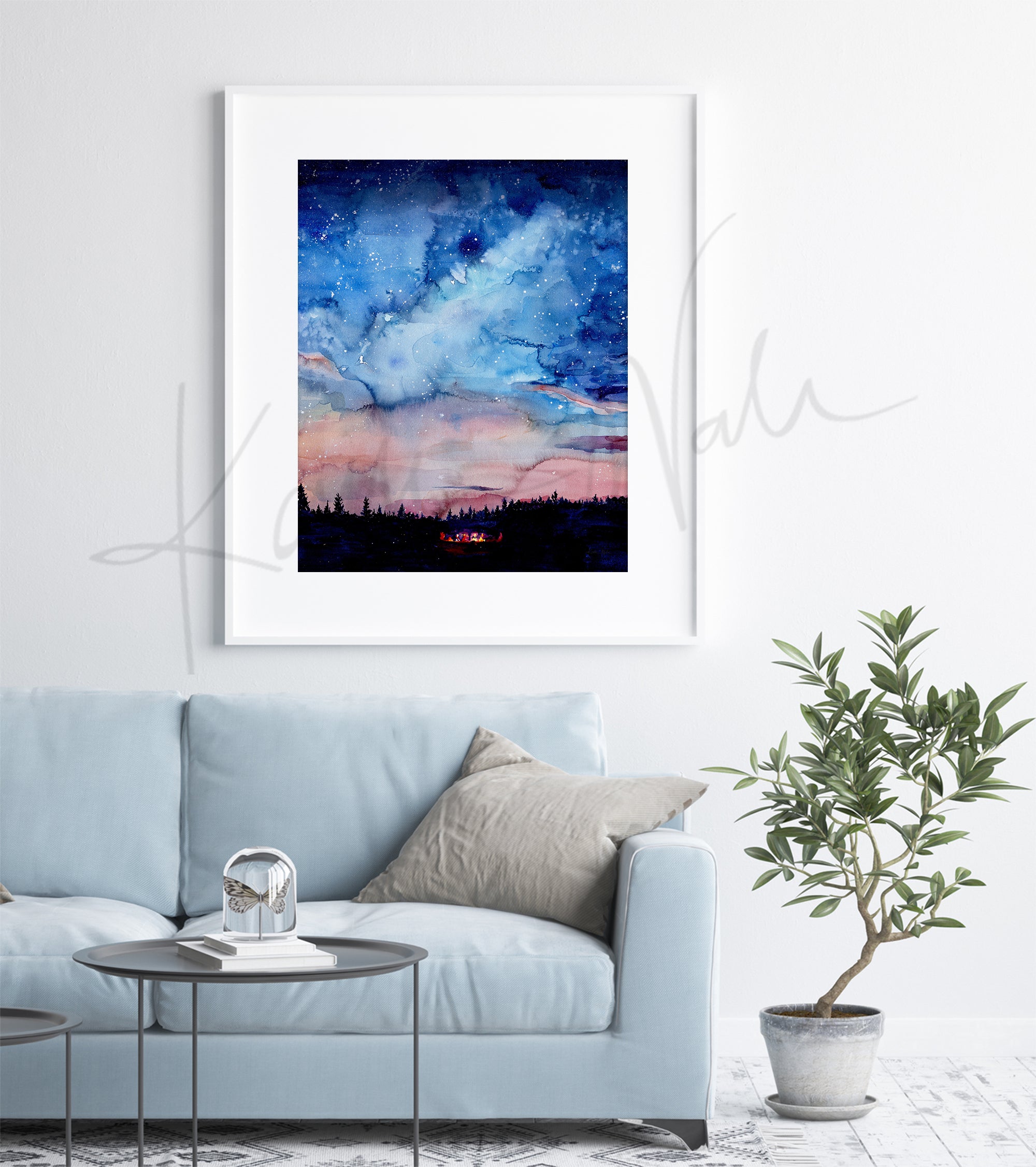 Framed watercolor painting of a bonfire, night sky, and silhouetted trees.. The painting is hanging over a blue couch.