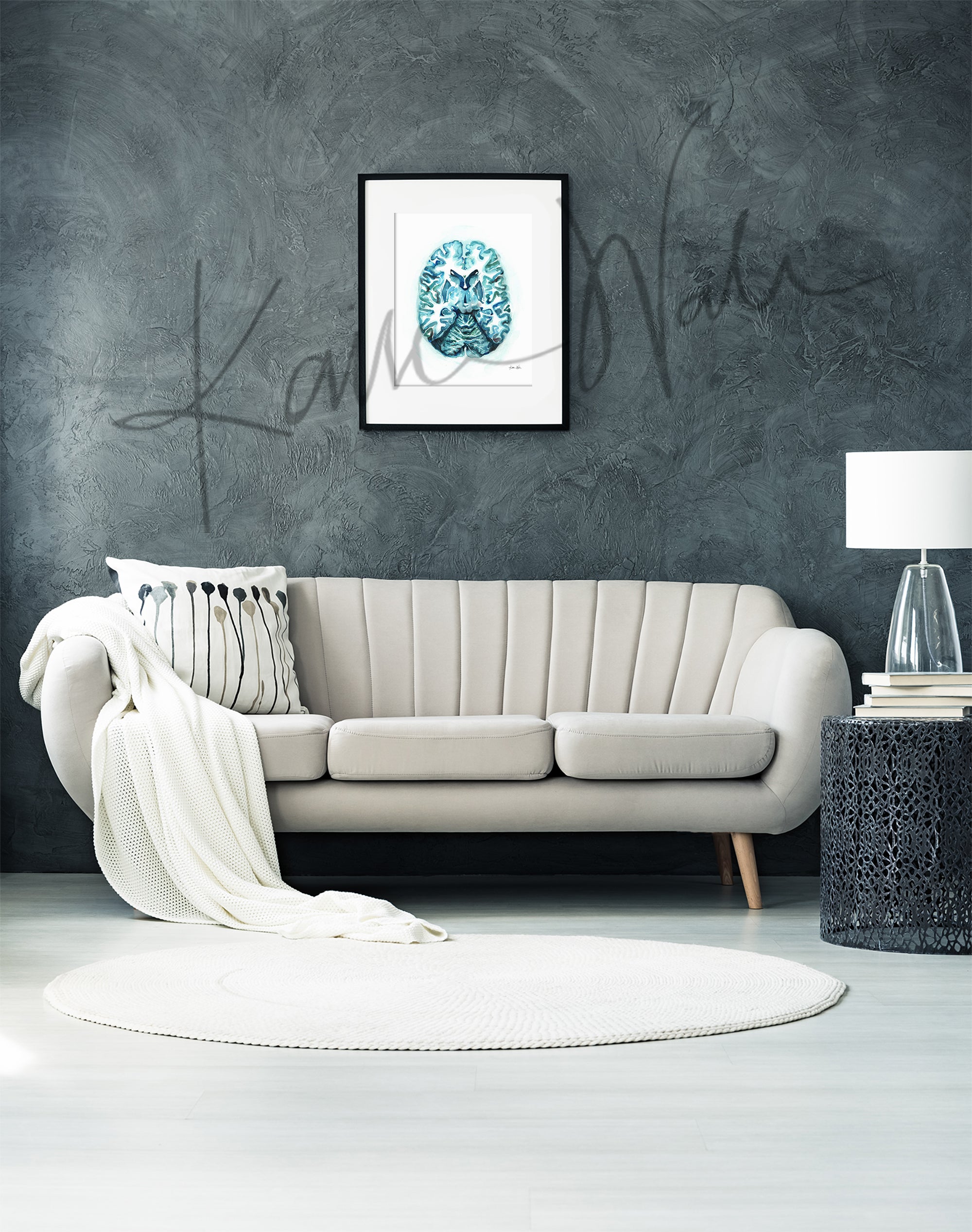 Framed watercolor painting showing a teal and blue transverse cut of the brain. The painting is hanging over a white couch.