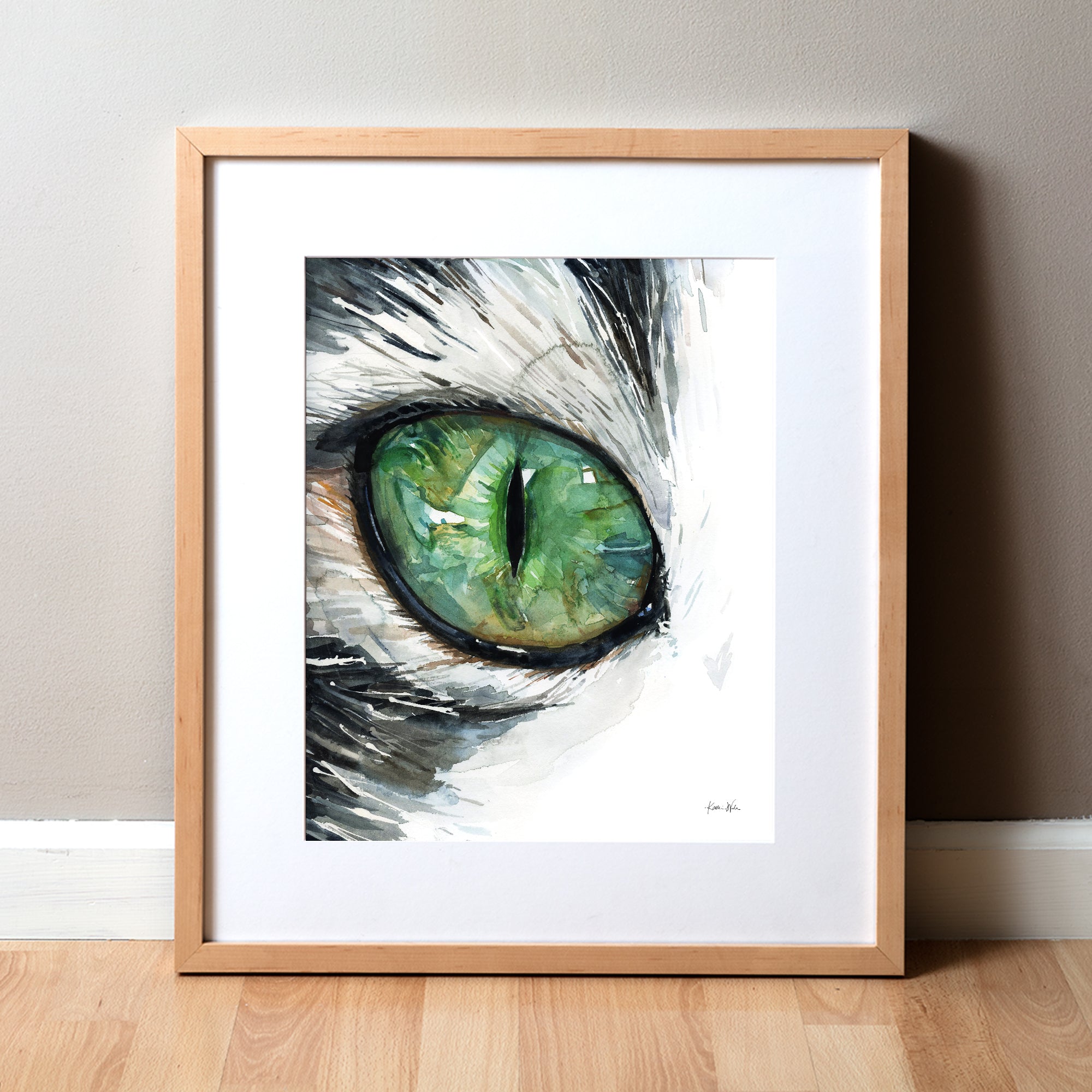 Framed watercolor painting of a zoomed in perspective of a green cat's eye. The hair surrounding the eye is black and white.