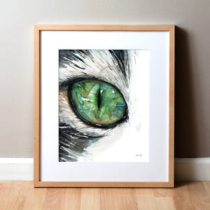 Framed watercolor painting of a zoomed in perspective of a green cat's eye. The hair surrounding the eye is black and white.