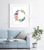 Framed watercolor painting of a flower wreath. The painting is hanging over a blue couch.