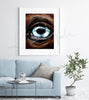 Framed watercolor painting of a zoomed in perspective of a horse eye. The iris is light blue and the horse is painted a warm brown. The painting is hanging over a blue couch.