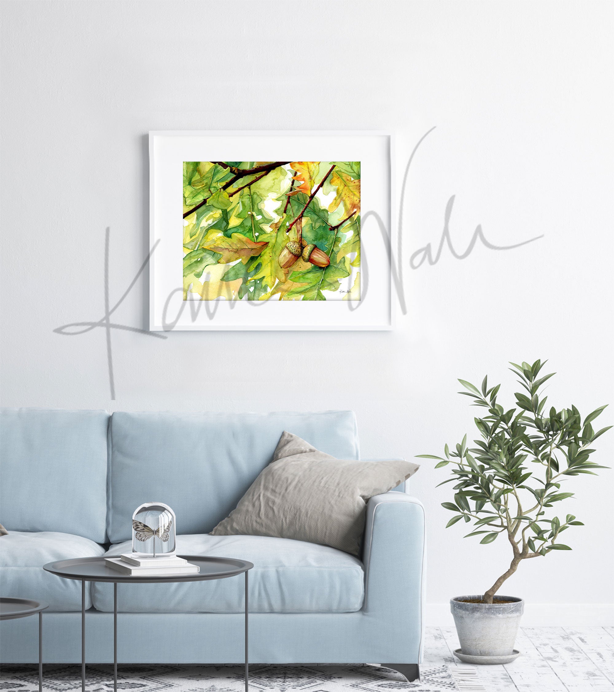 Framed watercolor painting of autumn leaves and acorns hanging from an oak tree. The painting is hanging over a blue couch.