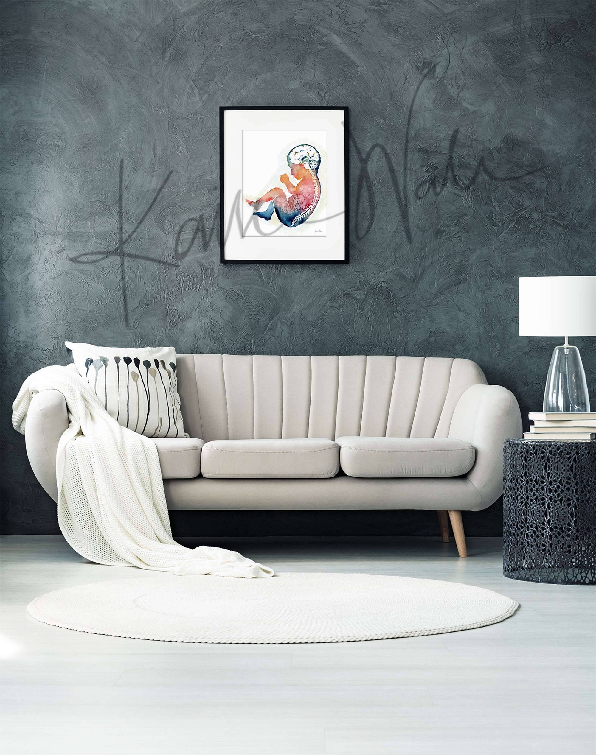 Framed watercolor painting of a fetus showing the spine and brain in rainbow colors. The framed print hangs above a beige couch.