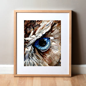 Framed watercolor painting of a zoomed in perspective of an owl eye. The iris is blue and feathers around the eye are painted in tans and browns.