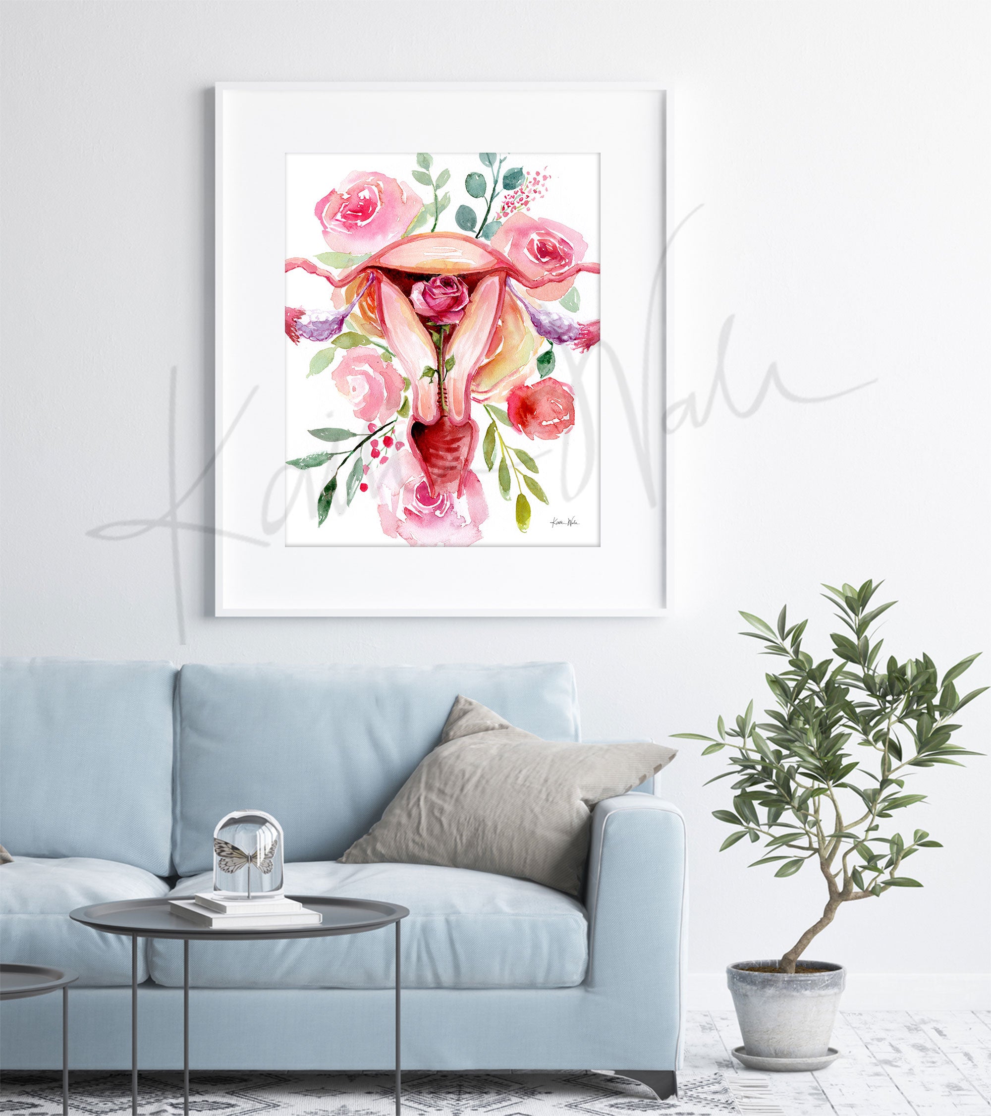 Framed watercolor painting of a uterus with flowers around. The painting is hanging over a blue couch.