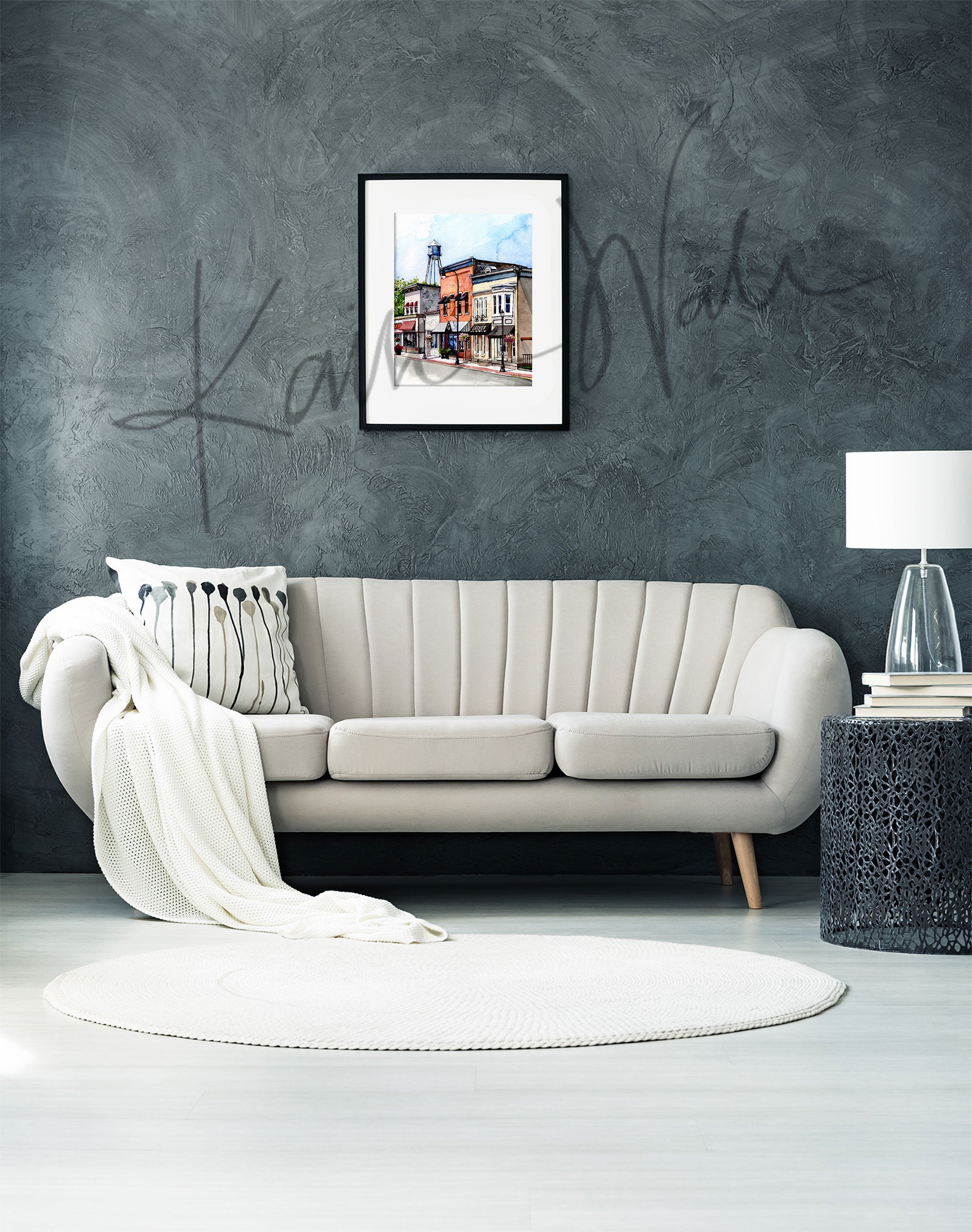 Framed watercolor painting of buildings on Main Street in Waunakee, Wisconsin. The painting is hanging over a white couch.